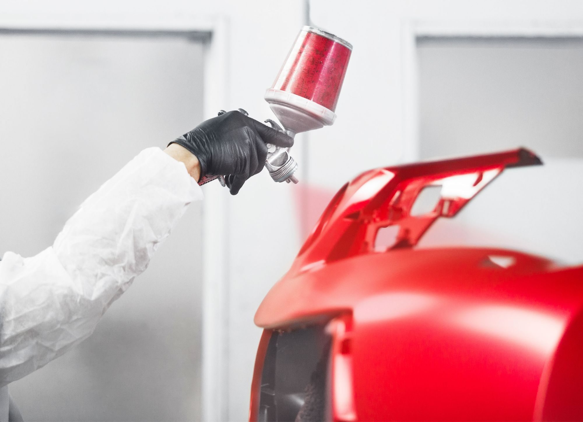 A person wearing PPE applies a red paint coating. 
